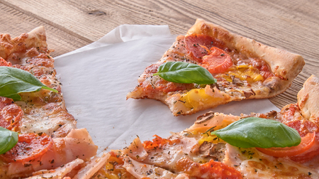 Delicious fresh pizza with ham and tomato on a wooden background.の写真素材