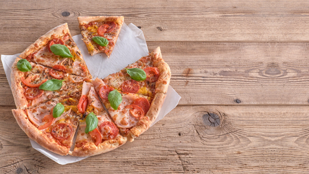 Delicious fresh pizza with ham and tomato on a wooden background.の写真素材