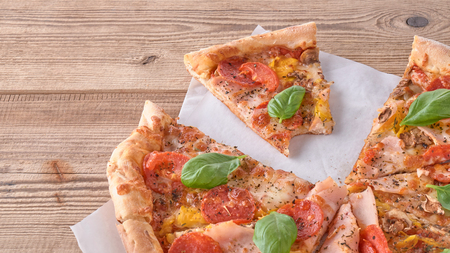 Delicious fresh pizza with ham and tomato on a wooden background.の写真素材