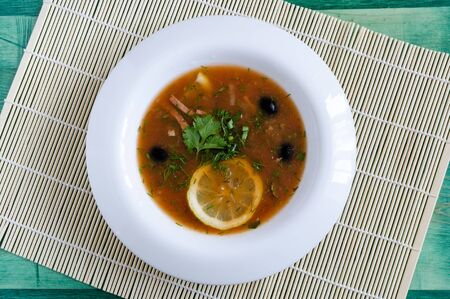 meat soup "Solyanka" in a white plate on a wooden background top viewの写真素材
