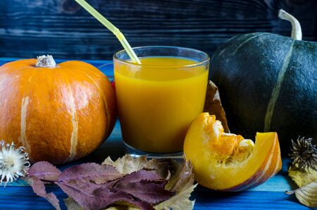 green and orange pumpkin and pumpkin juice in transparent bowl on wooden backgroundの写真素材