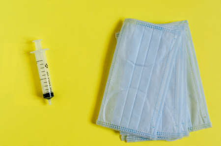 Syringe and protective masks on a yellow background top viewの写真素材