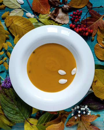 pumpkin soup in a white plate on a wooden background decorated with branches and leaves autumn themeの写真素材