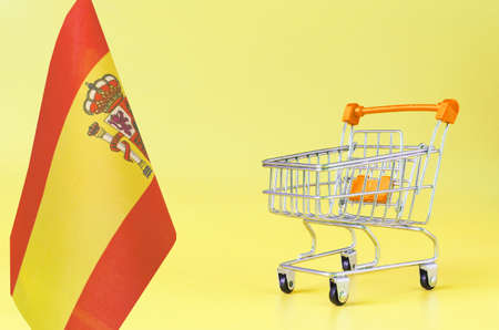 Empty shopping cart from the store and the Spanish flag on a yellow background concept consumer basket of Spainの写真素材