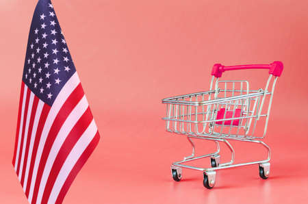 Empty metal shopping basket and the flag of the United States of America on a colored background consumer basket conceptの写真素材
