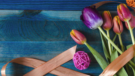 flatly floral arrangement of red-yellow and burgundy tulips with decor on a colored wooden backgroundの写真素材