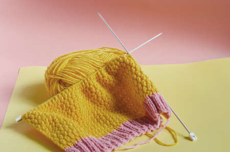 skein of bright yellow yarn on with knitting needles on a colored background needlework on the...