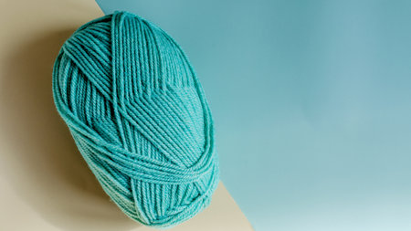 A ball of green yarn on a colored beige-turquoise background close-up, knitting concept.の写真素材