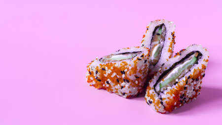 Fresh fish, cucumber and cheese rolls decorated with sesame and ginger on a pink background close-up. Red rolls kopi spaceの写真素材