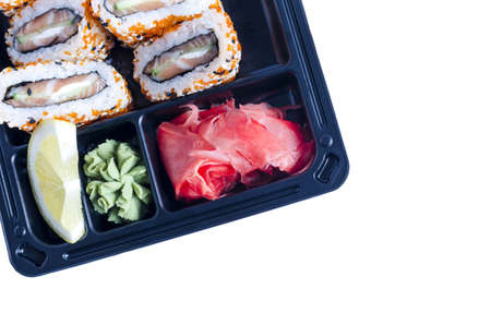 Fresh rolls of fish, cucumber and cheese, with ginger and wasabi in a dark plastic bowl close-up....