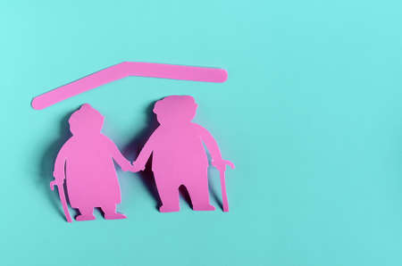 Bright red figures of two elderly people on a colored background. The concept of social protection of the elderly. Cardboard figures of elderly people pensionersの写真素材