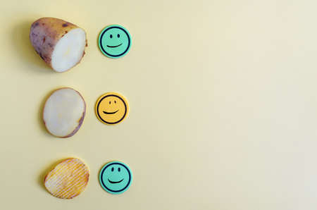 The concept of turning potatoes into chips. Potatoes, a slice of potato and fluted chips close-up on a yellow background. Potatoes and chips with colored painted faces close upの写真素材