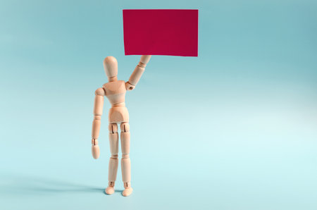 Figure of a wooden man with a red poster in his hand. The figure of a standing wooden man on the light background of the space mine.の写真素材