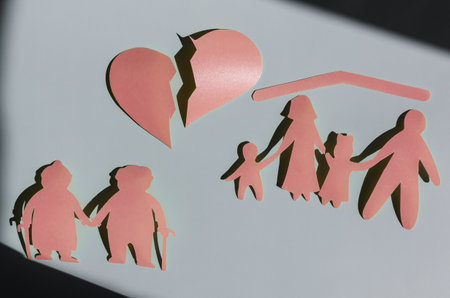 Red human figures of a divided family, a large heart divided into two parts on a colored background. The concept of the crisis of family relations. Cardboard figures of elderly people and adultsの写真素材