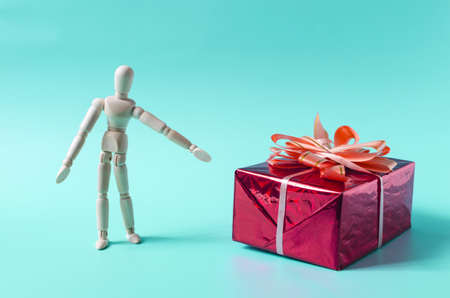 The figure of a wooden man pointing with his hand at a gift box. The figure of a wooden man and a large red box with a bowの写真素材