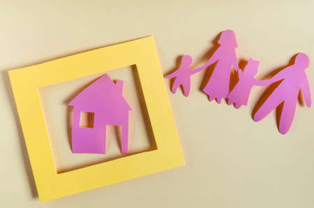 Bright red human figures and a house in a yellow frame on a light background. The concept of family and mortgage. Cardboard figures of adults and children close-up concept of a housing problemの写真素材