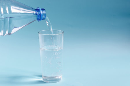 A plastic bottle that pours water into a glass glass on a colored background. A glass of clean water...