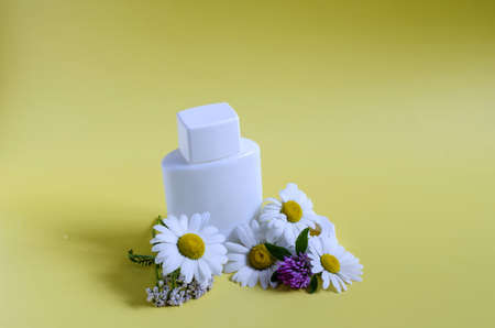 Chamomile flowers and a white bottle with a lid on a yellow background. Flowers with white petals and cosmetics on a light backgroundの写真素材