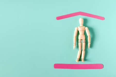 A wooden figure of a man under protection in the form of red frames on a colored background. The concept of social protection of the population, social problems.の写真素材