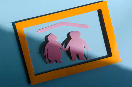 Bright red figures of two elderly people in a colored frame on a light background. The concept of social and insurance protection of the elderly. Cardboard figures of elderly people pensionersの写真素材