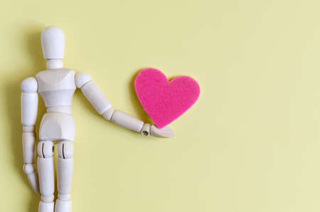 A figure of a wooden man with a heart on his outstretched arm. Concept valentine a man and a heart on a yellow background close-upの写真素材