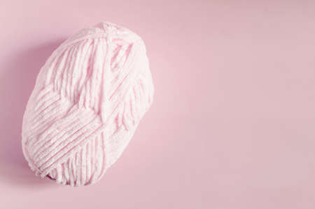 A skein of light pink yarn on a pink background top view is a place for text. An object for creativity and knitting a ball of pink threadの写真素材