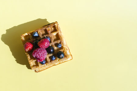 A waffle with different berries of black and red color on a yellow background is hard light....