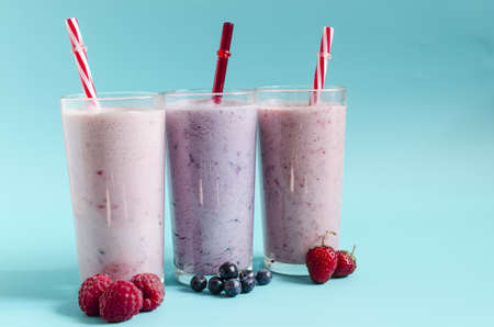 Milkshakes with the addition of raspberries, strawberries and blueberries on a light background close-up. Cocktails made of ice cream, milk and berries on a blue backgroundの写真素材