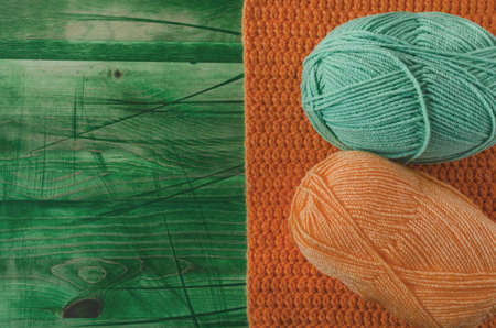 Balls of colored yarn on a green wooden background top view knitting concept. Colored yarn of orange...