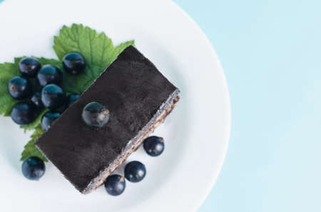 Cake with brown cream and black currant leaves and berries on a white plate top view. Black berries and a cake on a colored backgroundの写真素材