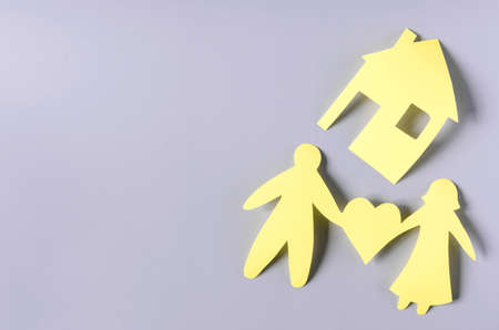 Cardboard figures of a man, a woman and a heart on a colored background. The concept of solving the housing problem of young families. Yellow cardboard figures of people and housesの写真素材