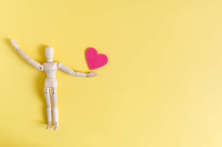 A wooden figurine holding a red heart at arm's length. Mannequin and heart on a bright yellow background of kopi spaceの写真素材