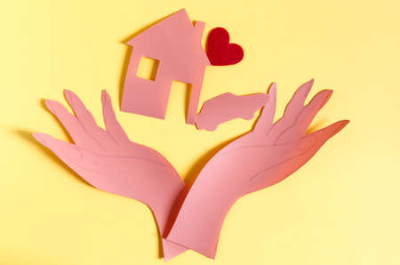 Two open palms made of red paper on a bright yellow background of kopi space. The concept symbol consists of two hands holding a house a car and a red heart a bright backgroundの写真素材