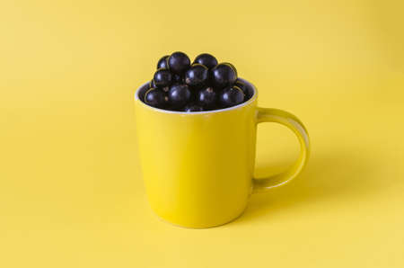 Black currant berries in a yellow circle on a yellow background close-up. Black berries in a bowl on a colored backgroundの写真素材
