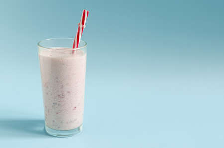 A milkshake in a transparent glass with a red tube on a bright blue background close-up. Cocktail of ice cream, milk and berries on a colored background place for textの写真素材