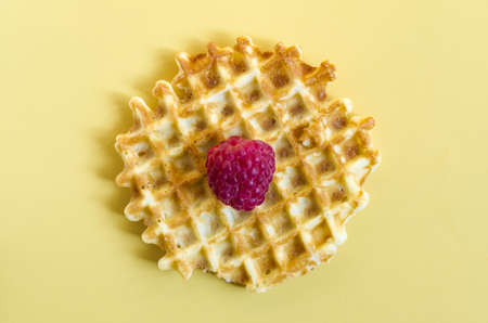 Waffle with a large raspberry berry on a yellow background close-up. Homemade cakes crispy waffle on a colored backgroundの写真素材