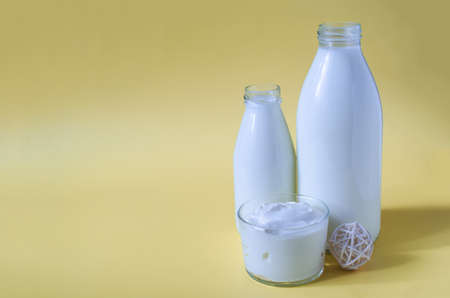 Sour cream in a glass container with milk bottles on a yellow background. Sour cream and dairy products in transparent dishes on a light background place for textの写真素材