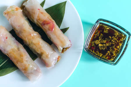 Spring rolls of seafood and vegetables with a decor of green leaves on a light background. Spring...