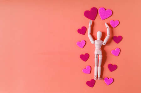 A wooden figure of a man holding a red heart above his head. Mannequin and hearts on a bright red...