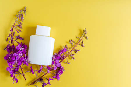 Lilac-colored wildflowers and a white bottle of cosmetics on a colored background. Flowers and...