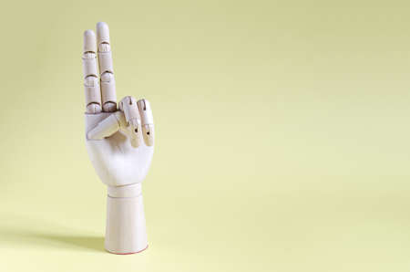 A wooden hand with two fingers raised up on a yellow background. Concept gesture wooden hand shows two fingers up.の写真素材