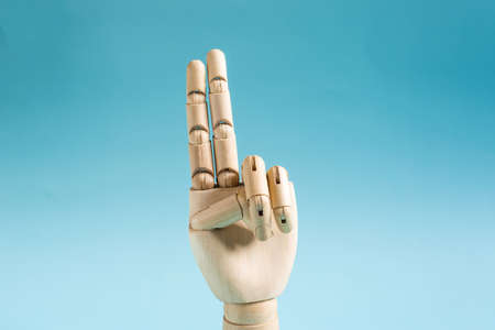 A wooden hand with two fingers raised on a blue background. Conceptual gesture number twoの写真素材