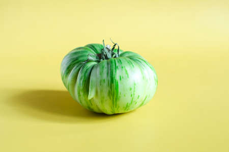 A green tomato on a yellow background of a copy space. Vegetable green tomato close-upの写真素材