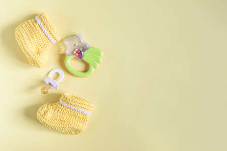 A set of things for a small child on a yellow copy space background. Knitted children's shoes, a toy and a pacifier on a light backgroundの写真素材