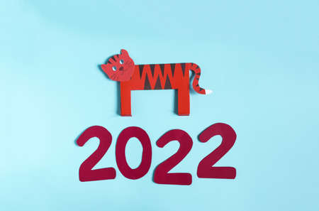Colorful paper tiger and the numbers 2022 on a light background. The symbol of the new year 2022 is...