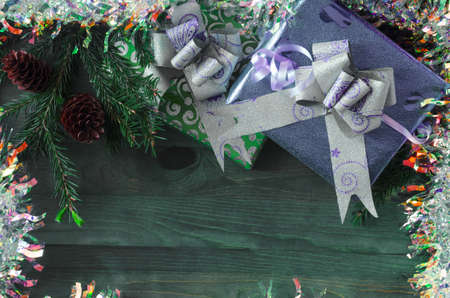 Christmas background a bright gift in a green package and a decor of fir branches and fir cones on a natural wood backgroundの写真素材