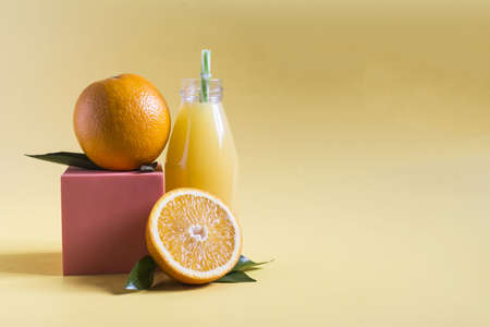 Fresh orange juice in a transparent glass with a decor of oranges and green leaves on a yellow background copy spaceの写真素材
