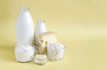 A set of dairy products in close-up on a yellow background is a place for text. Milk, kefir, sour cream, cheese, butter and cottage cheese in a transparent bowl on a light backgroundの写真素材