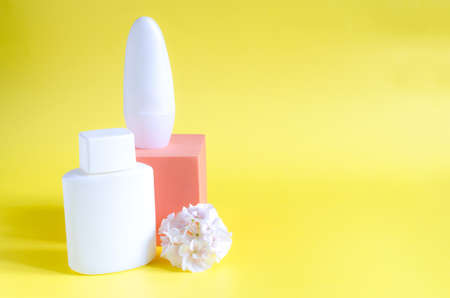 Body and skin care products in white packaging on a yellow background. Flowers and cosmetics on a...