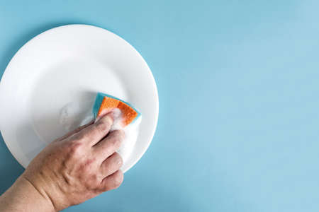 Action the hand holds a sponge with foam on a clean white plate. The concept of washing dishes and...